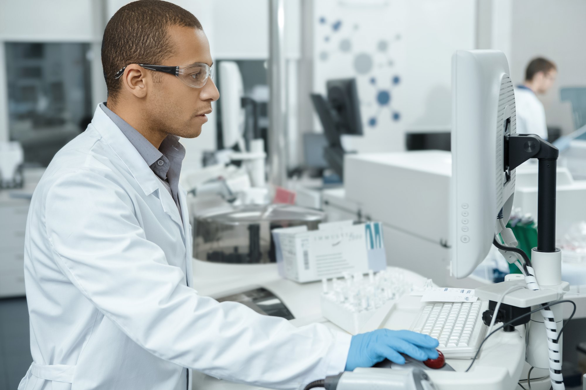 A man in a lab coat is focused on his work while using a computer in a laboratory setting. A man in a lab coat is focused on his work while using a computer in a laboratory setting.